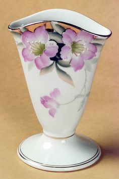 a white vase with pink flowers painted on the front and bottom, sitting on a tan surface