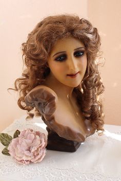 a close up of a doll on a table with a flower in her hair and dress