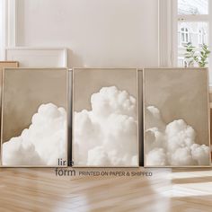 three canvases with white clouds on them in front of a window and wood floor