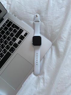 an apple watch sitting on top of a laptop computer next to a white cloth covered bed