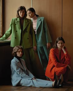 three women sitting on the floor in front of a wall wearing green and orange coats