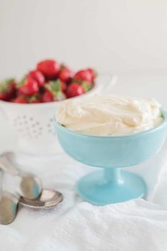 a bowl of whipped cream next to a bowl of strawberries on a white tablecloth