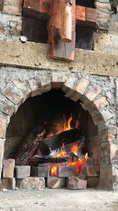 a brick oven with fire burning in it's door and logs on the outside