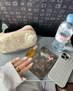 a woman's hand is holding an empty water bottle next to her purse and other personal items