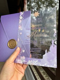 a person holding up a purple and gold wedding card with a wax stamp on it