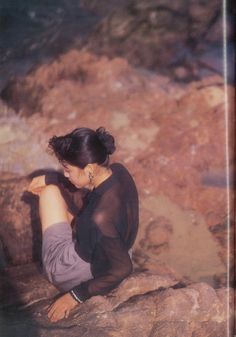 a woman sitting on top of a rock next to water