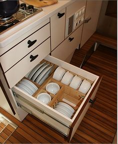 an open drawer in the middle of a kitchen with plates and bowls inside on it