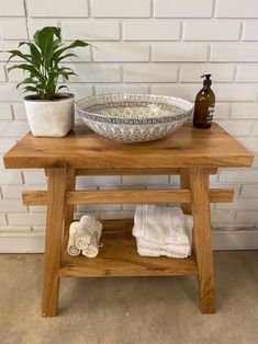 a wooden table with a bowl on it and two towels under the sink, next to a potted plant