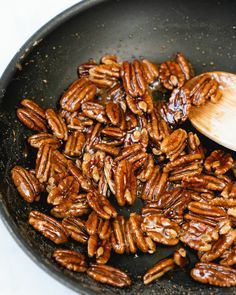 pecans being cooked in a skillet with a wooden spoon