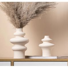 two white vases sitting on top of a table next to each other with dried grass in them