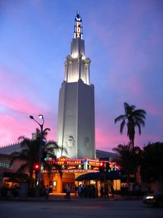 a very tall tower with a clock on it's side at dusk in front of palm trees