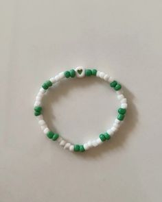 a white and green beaded bracelet with heart charm on the end, sitting on a table