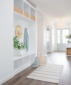 a hallway with white walls and wooden floors, baskets on the wall, and a rug in front of it