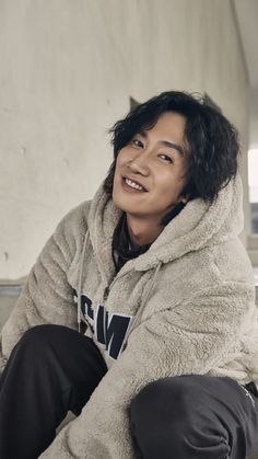 a young man sitting on the ground wearing a hoodie and smiling at the camera