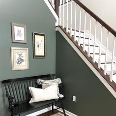 a black bench sitting under a stair case next to a white bannister and framed pictures on the wall