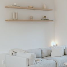 a living room with white couches and wooden shelves on the wall above them is lit by two lamps