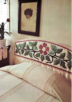 a bed with a flowered headboard and pillow on it next to a painting