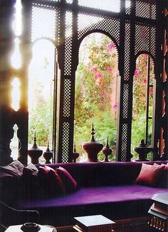 a purple couch sitting in front of a window next to a table with two vases on it