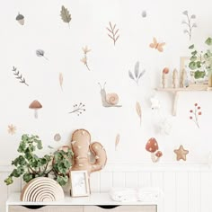 a white dresser with flowers and butterflies on the wall next to a potted plant