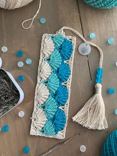 a crochet bookmark with blue and white yarn next to it on a wooden table