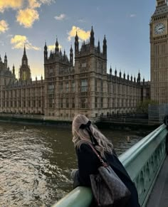 a woman standing on the edge of a bridge looking at big ben