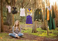 a woman sitting on the ground in front of some clothes hanging from a line and smiling