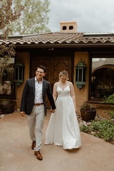 a bride and groom walking in front of a house with an adobe - style roof