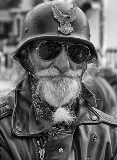 an old man with a beard wearing a motorcycle helmet and bandana on the street