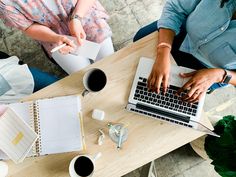 three people sitting at a table with laptops and papers on top of the desk