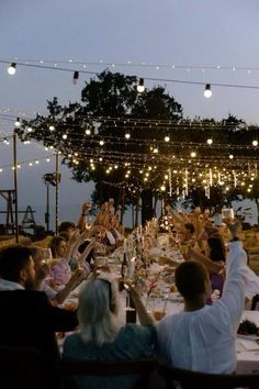 a group of people sitting around a dinner table with lights strung over the top of it