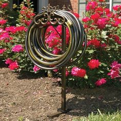 there is a metal sculpture in the middle of some bushes and pink flowers near a house