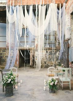 an outdoor area with chairs, tables and white draping hanging from the ceiling