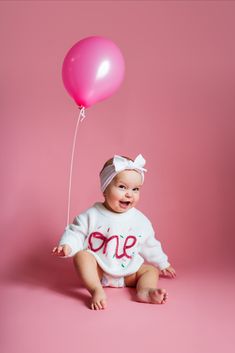 a baby sitting on the ground with a pink balloon