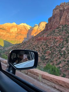 a woman taking a selfie in the side mirror of a car with mountains in the background