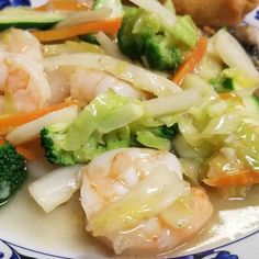 shrimp, broccoli and carrots are on a plate with bread in the background