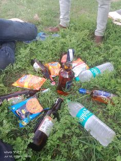 there are many bottles and cans on the ground with people sitting in the grass behind them