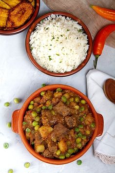 three bowls filled with rice, peas and meat next to carrots on a table