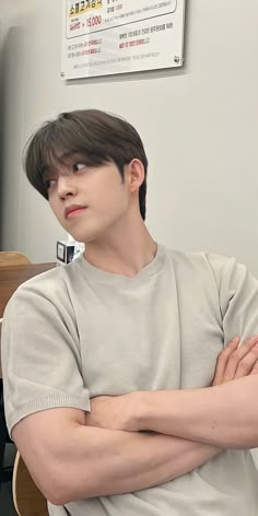 a man with his arms crossed sitting in front of a computer desk and monitor screen