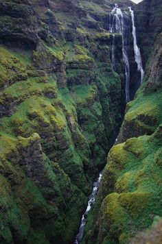 a large waterfall in the middle of a lush green mountain valley with moss growing on it's sides