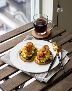 an open face sandwich with shrimp and eggs on a plate next to a cup of tea