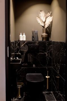 a bathroom with black marble and gold accents, including a plant on the counter top