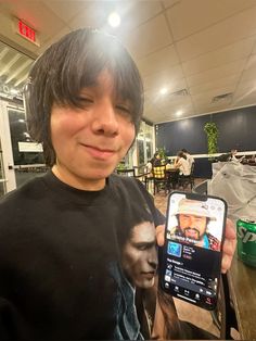 a young man holding up a cell phone in his right hand and smiling at the camera