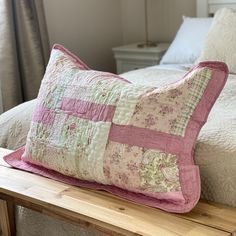 a pink and green patchwork pillow sitting on top of a wooden bench next to a bed