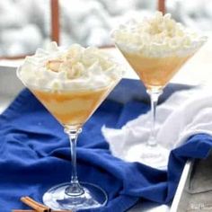 two glasses filled with dessert sitting on top of a blue table cloth next to cinnamon sticks