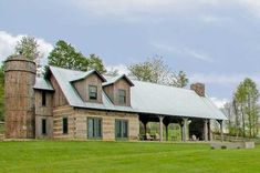 an old log house with a metal roof and covered porch in the middle of a grassy field