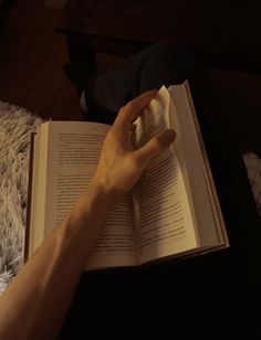 a person is reading a book while laying on a bed with their hand resting on an open book