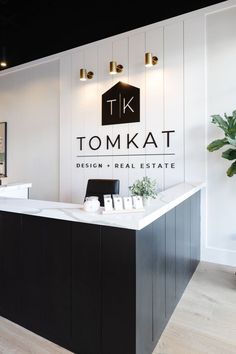 the front desk of a business with black and white walls, wood flooring and lighting