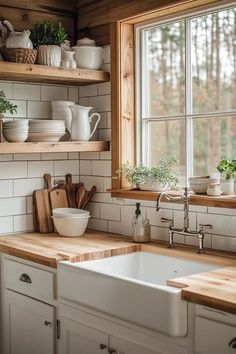 a white kitchen sink sitting under a window next to a wooden shelf filled with dishes