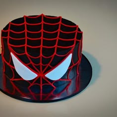 a spiderman cake with red and black icing on it's face, sitting on a plate