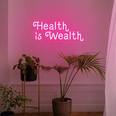 there is a neon sign that says health is wealth on the wall next to two potted plants